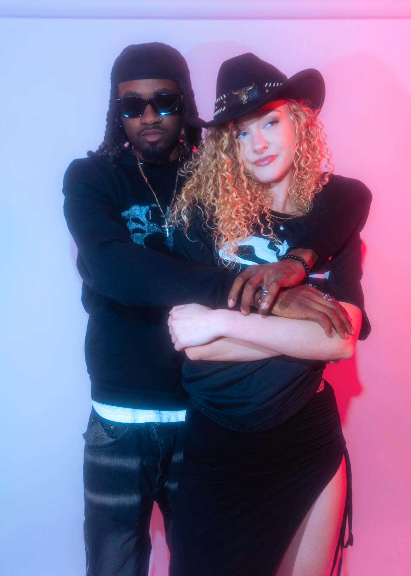A two-up lookbook frame in saturated pink: a Lone Star Noir tee, a longhorn-banded cowboy hat, peace signs thrown into colored gel. Streetwear shot like a record cover.