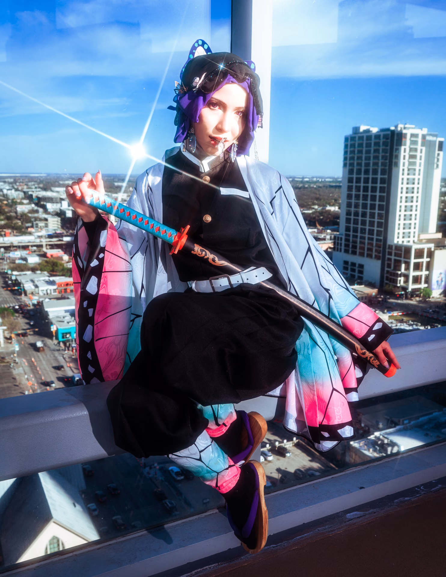 Shinobu Kocho perched on a high-rise ledge, butterfly haori and katana against an Austin skyline and hard blue sky; convention cosplay shot like a magazine cover.