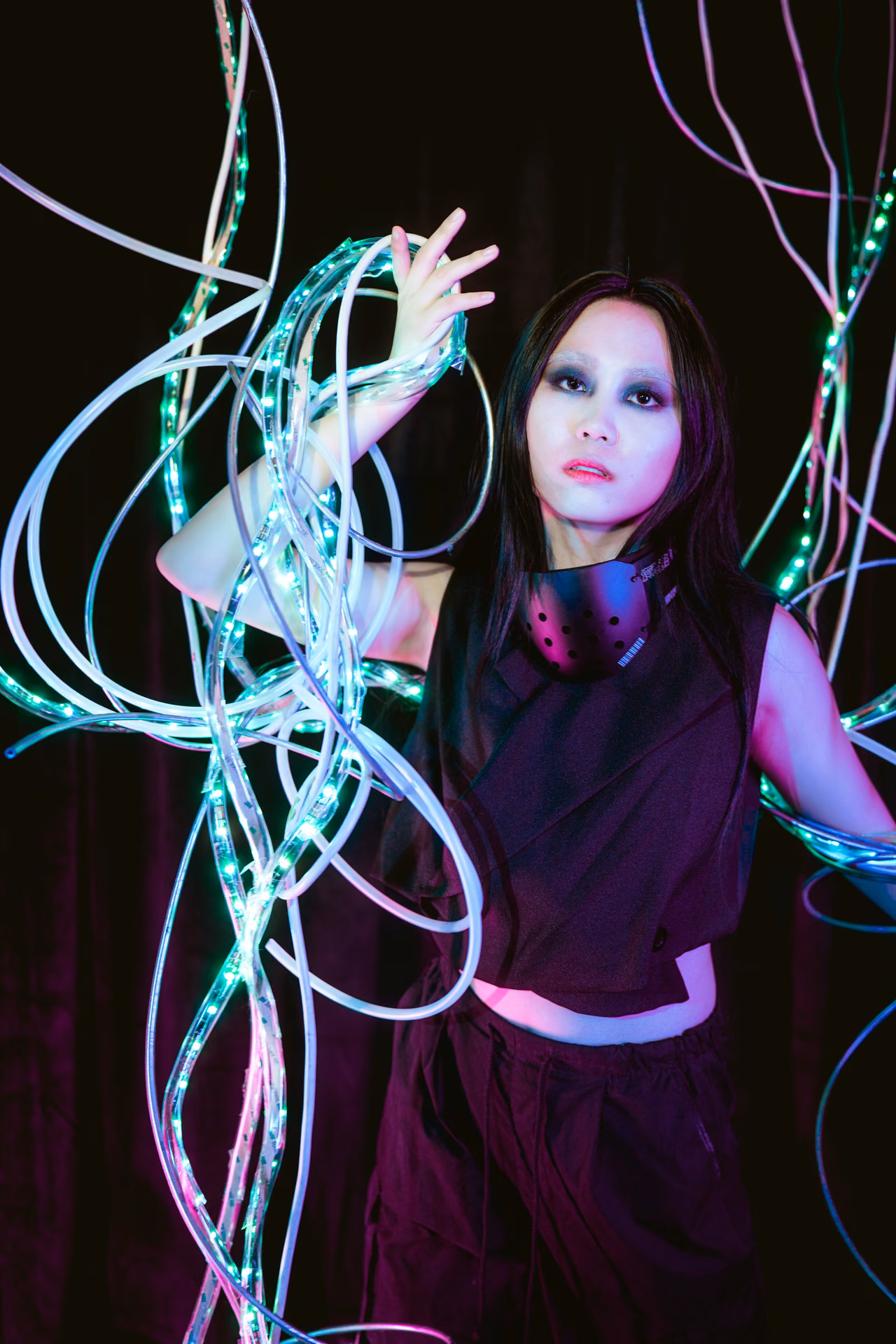 Three figures laced in fiber-optic light stand in a red-and-green wash — part of Davila's conceptual Automated Art series, the wires both costume and circuitry.