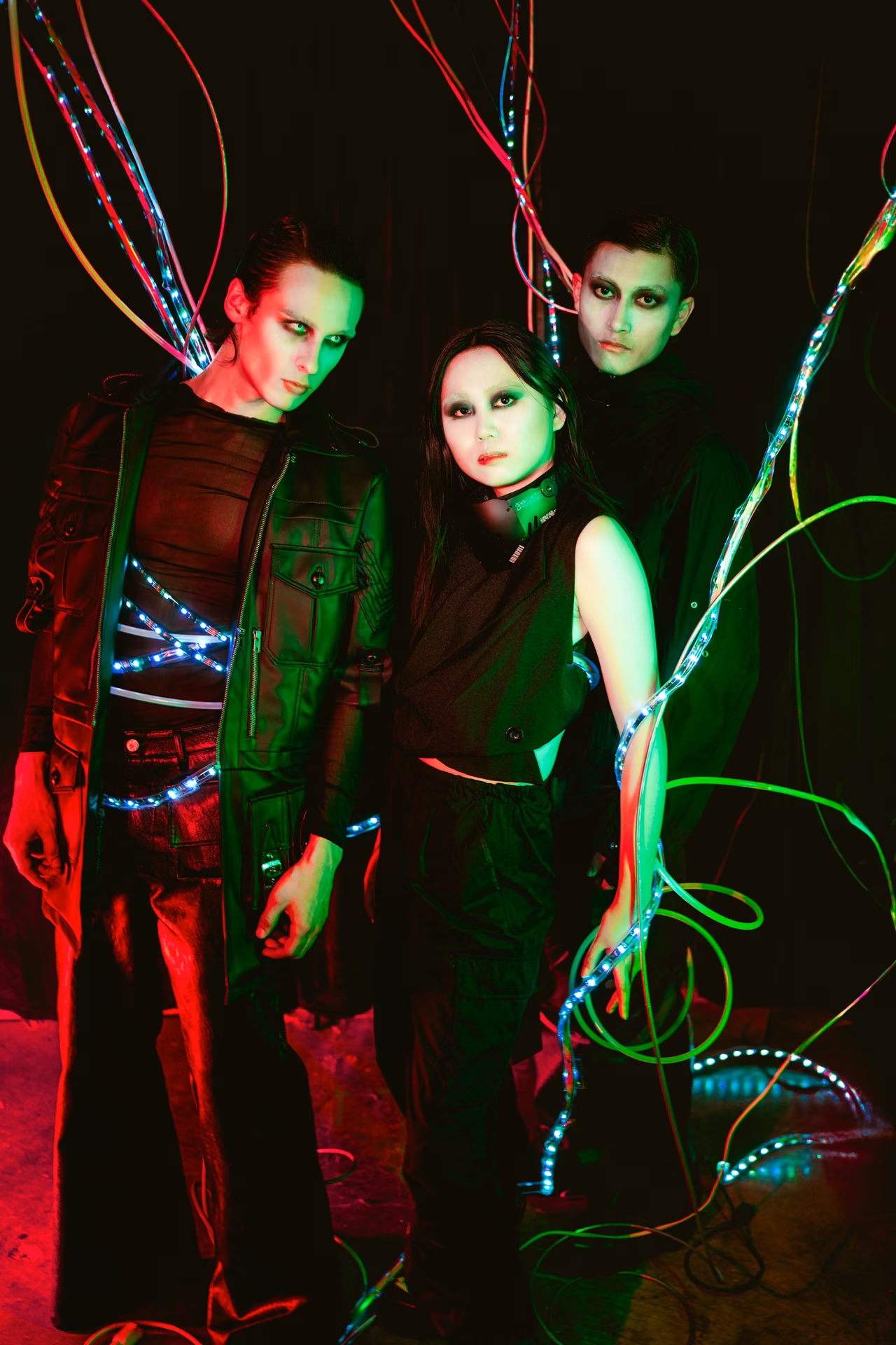 Three figures laced in fiber-optic light stand in a red-and-green wash — part of Davila's conceptual Automated Art series, the wires both costume and circuitry.