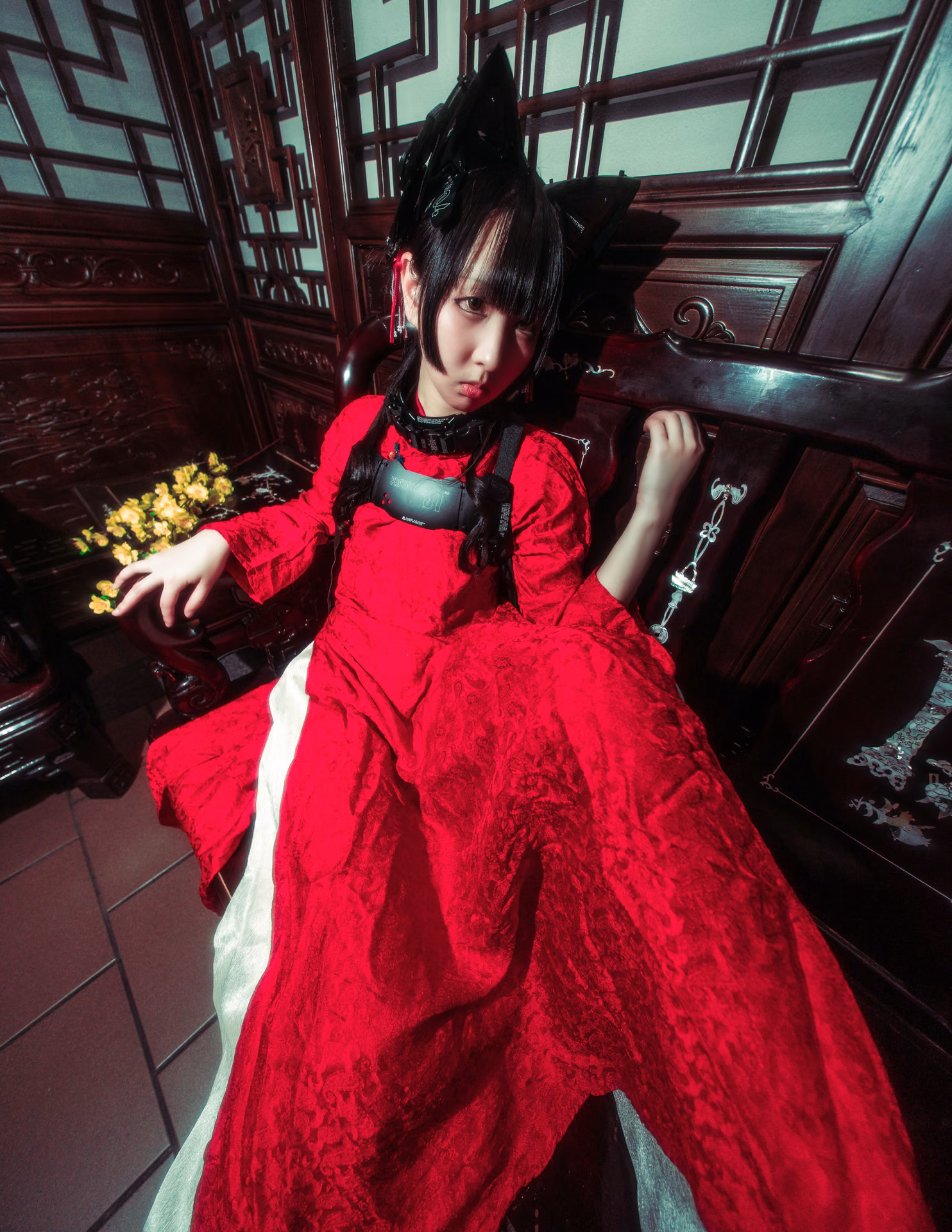Under red lanterns on a mall staircase, a cat-eared figure in red lace cradles a branch of yellow blossom; a wide-angle frame that lets the location's color carry the mood.