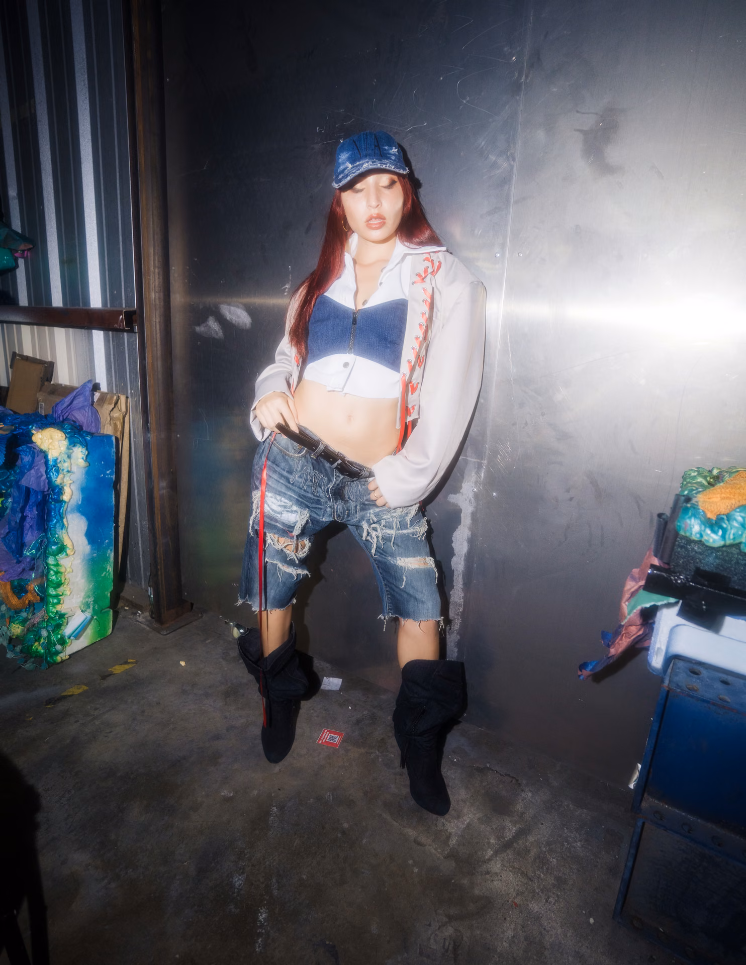 A pink off-shoulder mini and black cowboy boots cross a warehouse runway past a fallen Greek column; Texas swagger caught inside the live-show frame.