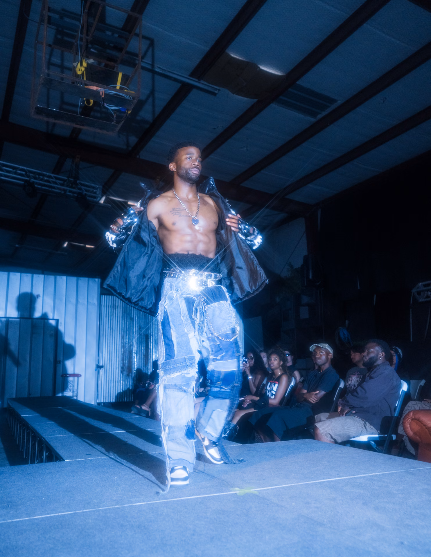 A pink off-shoulder mini and black cowboy boots cross a warehouse runway past a fallen Greek column; Texas swagger caught inside the live-show frame.