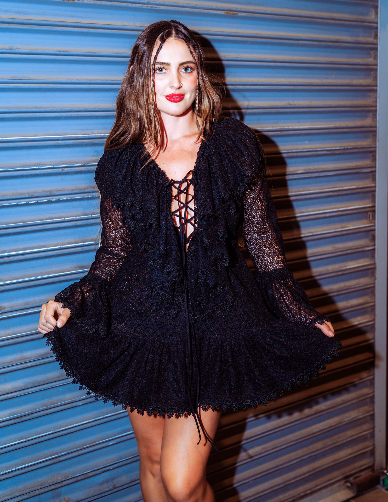 Flash hits wet auburn hair and a swirl of white lace against a metal shutter — a night-alley editorial caught mid-motion, romantic and a little feral.