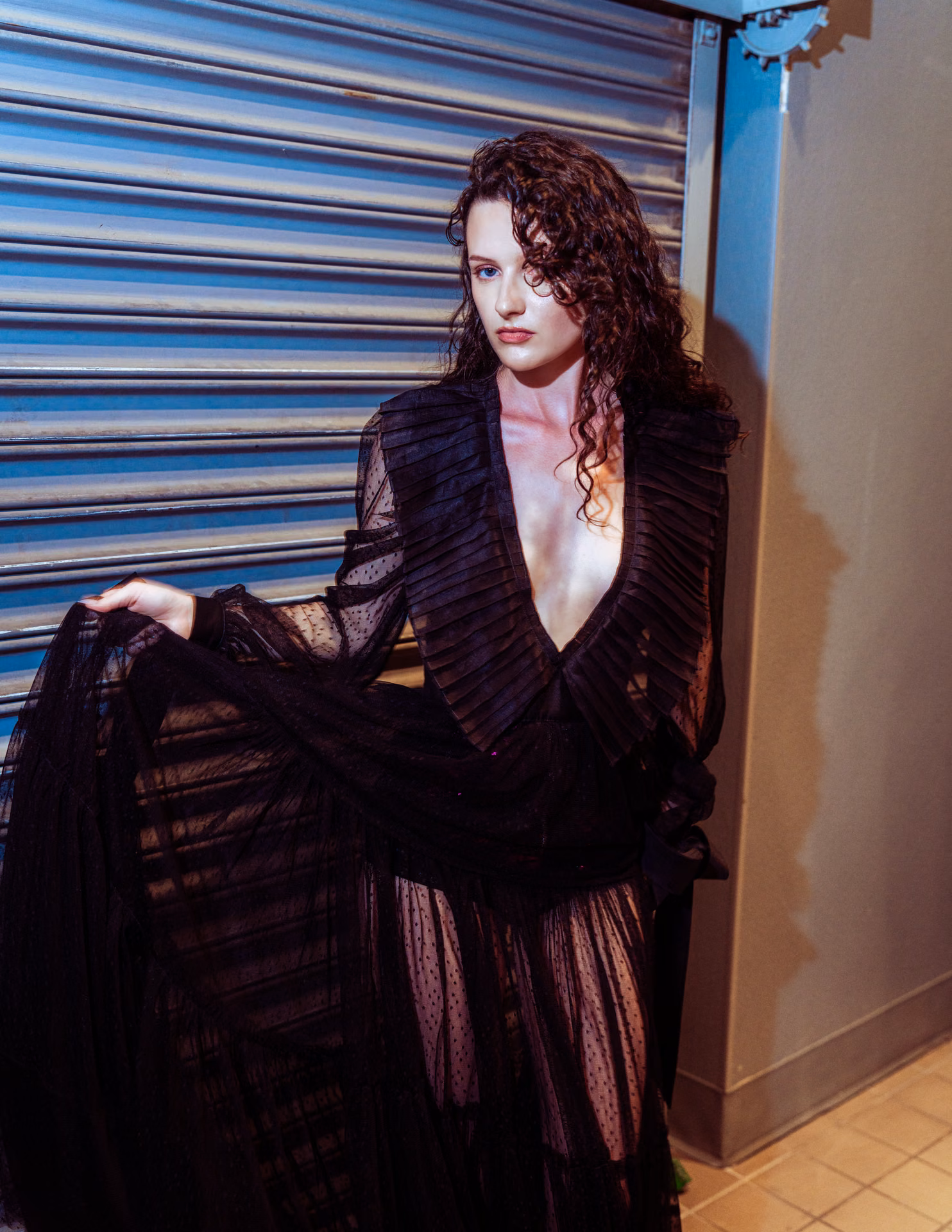 Flash hits wet auburn hair and a swirl of white lace against a metal shutter — a night-alley editorial caught mid-motion, romantic and a little feral.